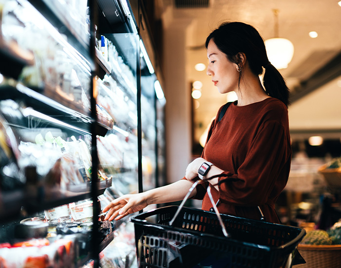 Woman shopping in a grocery store aisle with a shopping basket