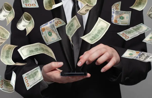 Person in suit works on mobile phone under money rain on grey background