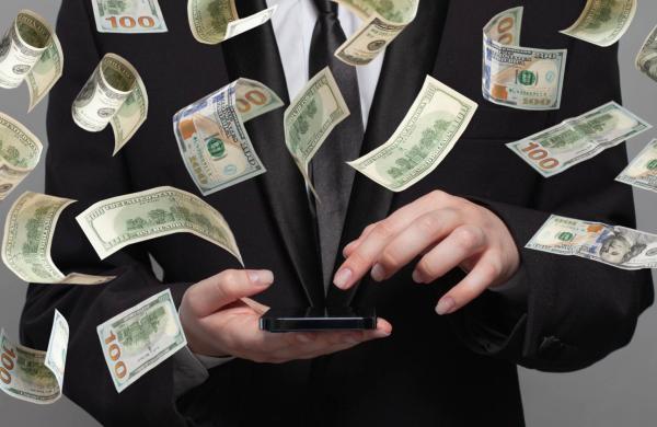 Person in suit works on mobile phone under money rain on grey background