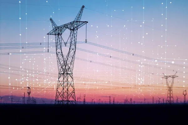 A large electrical transmission tower stands against a sunset sky with a smaller tower in the distance.