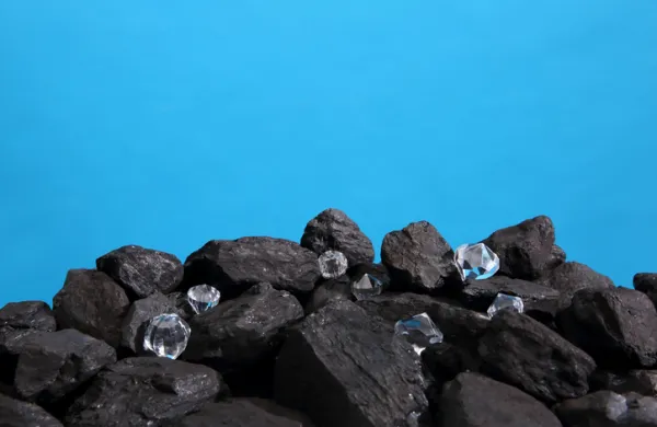 Black coal is strewn on a prism on a blue background and among it there are polished diamonds.