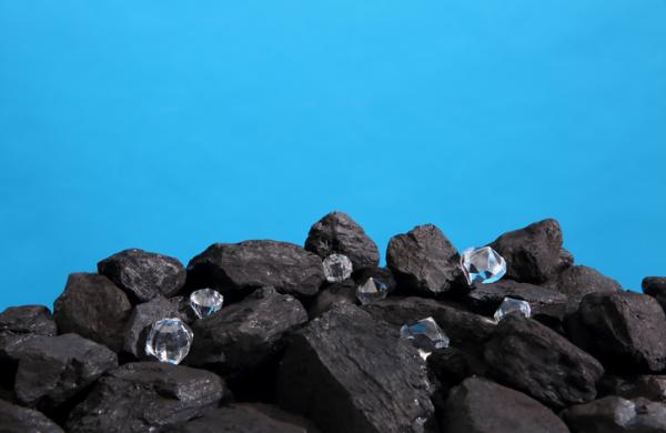 Black coal is strewn on a prism on a blue background and among it there are polished diamonds.