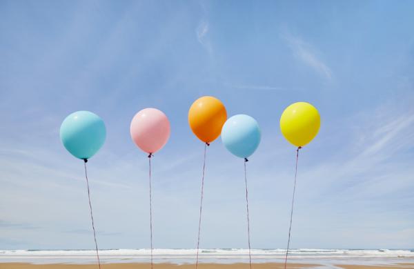 Five colorful balloons in a row at beach against blue sky