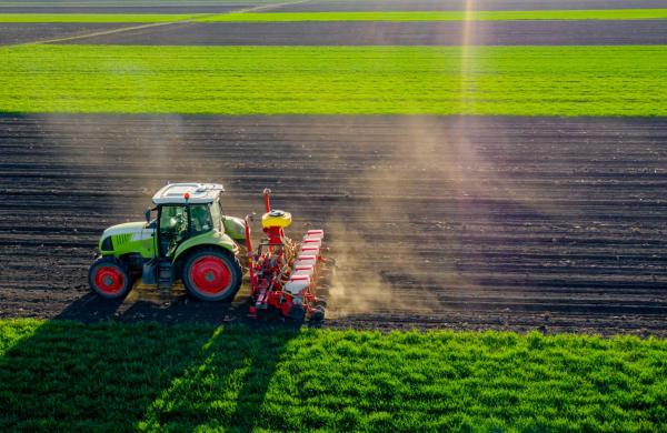 Aerial view of tractor as dragging a sowing machine over agricultural field, farmland