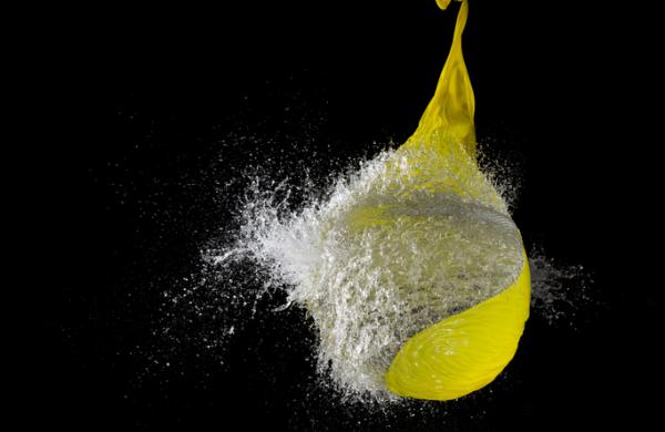 Yellow waterballoon bursting against black background, close up