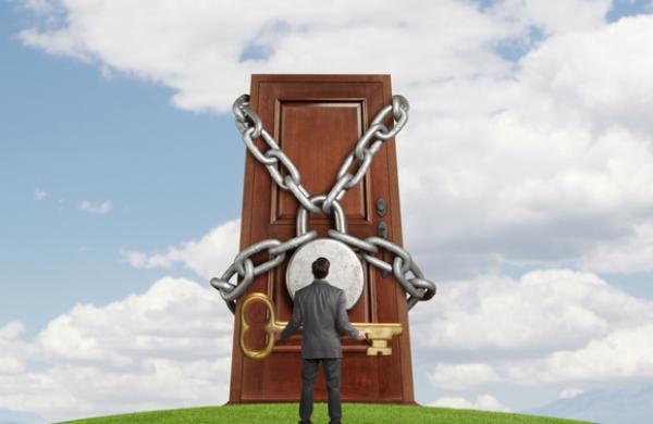 Businessman holding large key looking up at padlocked door
