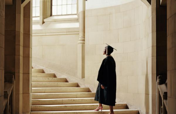 Women wearing graduation cap and gown, ascending staircase, rear view