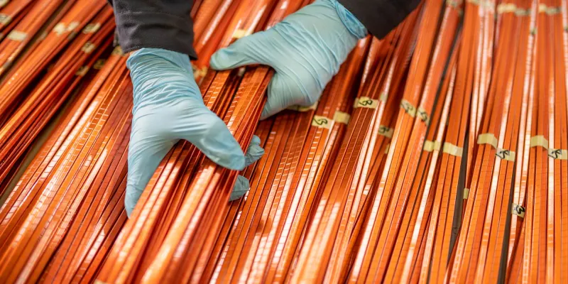 Two hands in blue gloves arranging orange copper pipes.
