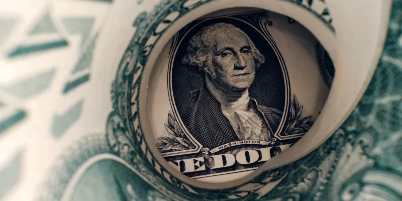 U.S. Dollar banknote seen through rolled-up One Dollar bill. Focus on George Washington. 