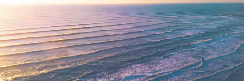 Aerial view of a calm ocean with gentle waves at sunset, pink and blue sky.