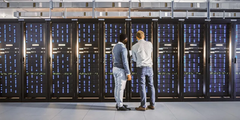 People working on a server room filled with rows of large computer racks.