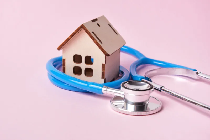 Medical stethoscope and toy house on a pink background with copy space