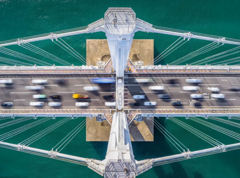 Aerial view of a bridge with cars crossing over water, viewed from above.
