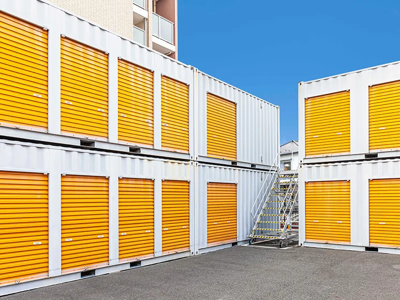 Stacked storage units with orange doors and yellow window shutters under a blue sky