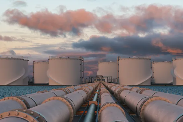 Industrial tanks and pipelines against a cloudy sky at sunset.